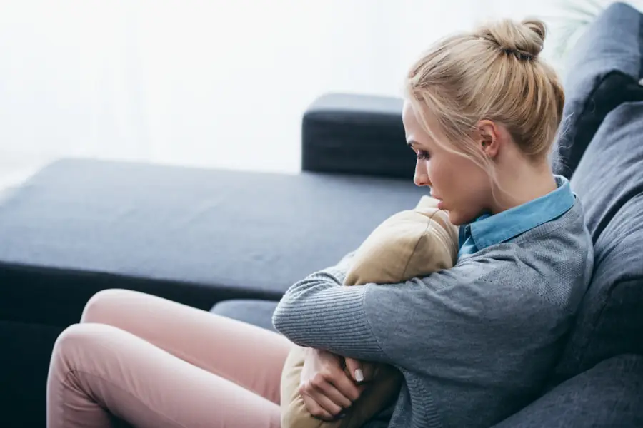 Woman sitting thoughtfully on sofa with pillow.